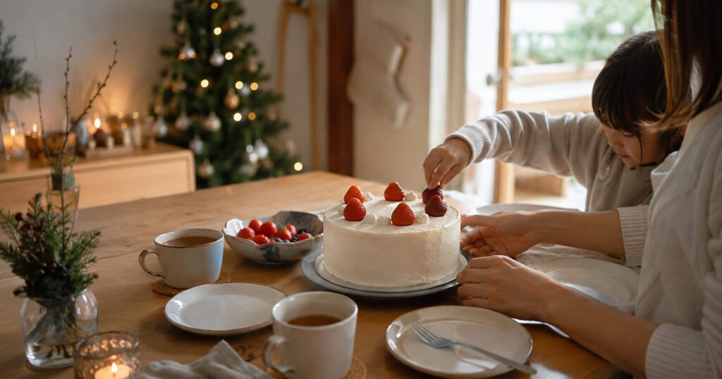 木のテーブルにクリスマスケーキと小皿、温かい飲み物を並べた家庭の食卓